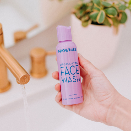 Frownies pH balancing face wash being held by hand shown over a bathroom sink