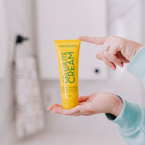 Frownies cellulite cream being held in a bathroom setting. Only the woman's hands are present in the photo