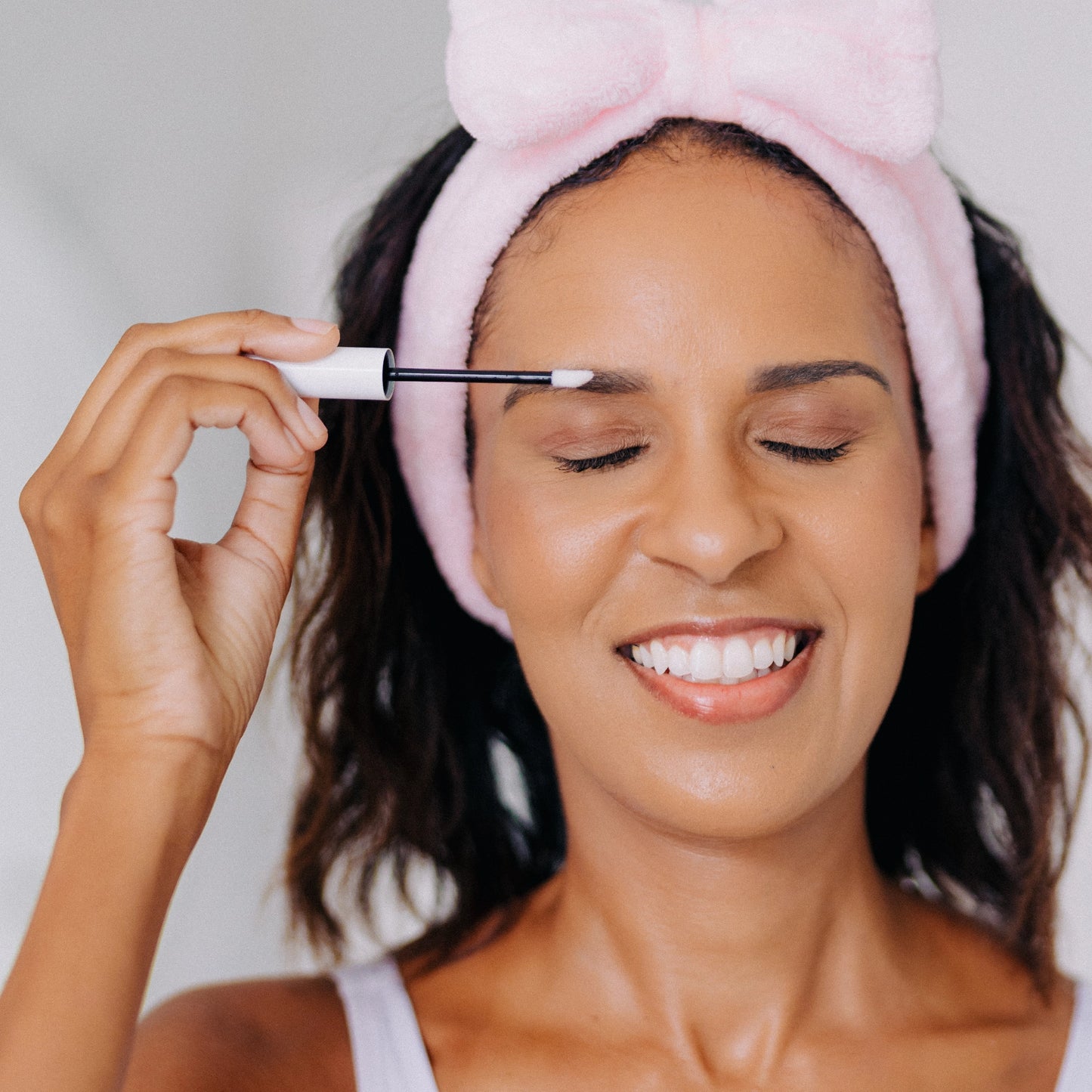 A happy woman applying Frownies Eyebrow Growth Serum while wearing a Frownies skincare headband