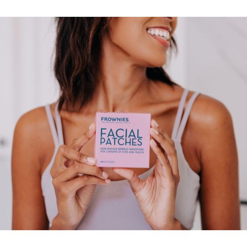 A happy girl is holding a box of Frownies CEM (corners of eyes and mouth) facial patches. She is smiling and looking directly at the camera, with the box prominently displayed in her hands