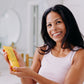 A woman with black hair shown holding the Frownies cellulite cream bottle in her hands and smiling