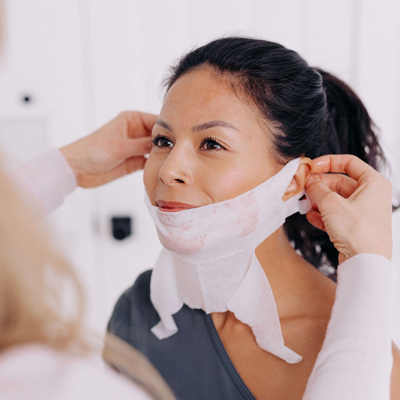 A woman with black hair having someone else put on her Frownies chin up polypeptide mask 