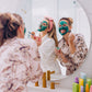 2 woman in the mirror applying Frownies blue green algae clay mask with the brushes, one woman is also wearing frownies skincare headband 