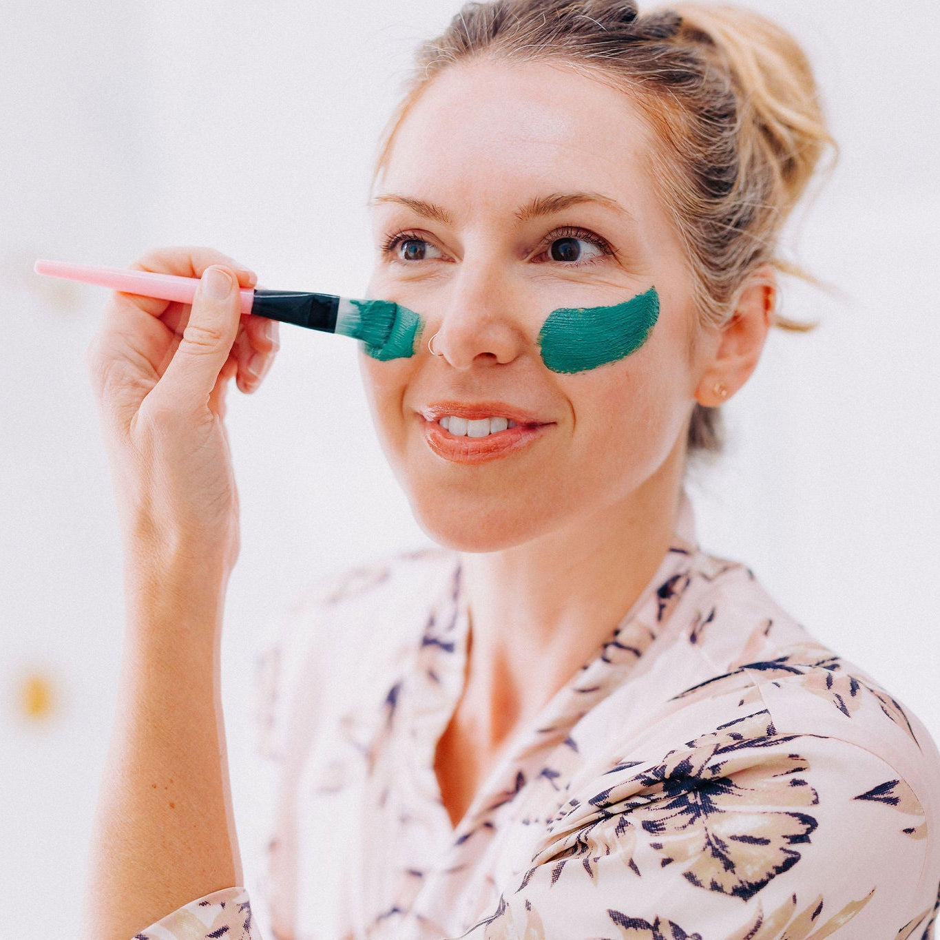 Frownies blue green algae clay mask being applied to a womans face with the brush 