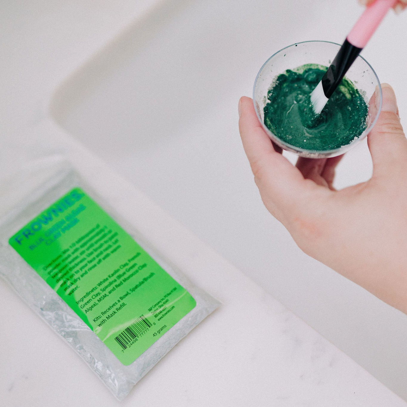 Frownies blue green algae clay mask shown being stirred in the cup to create the final form of the mask before it is applied to the skin 