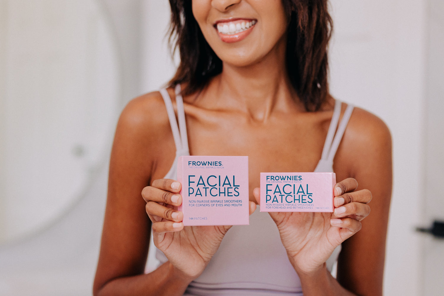 a closeup of a woman who is holding 2 frownies facial patches boxes in her hand