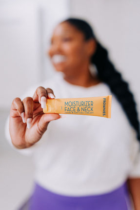 Frownies moisturizer for face and neck with aloe and oat gel cream pictured with a black woman holding the orange container in her hands and smiling 