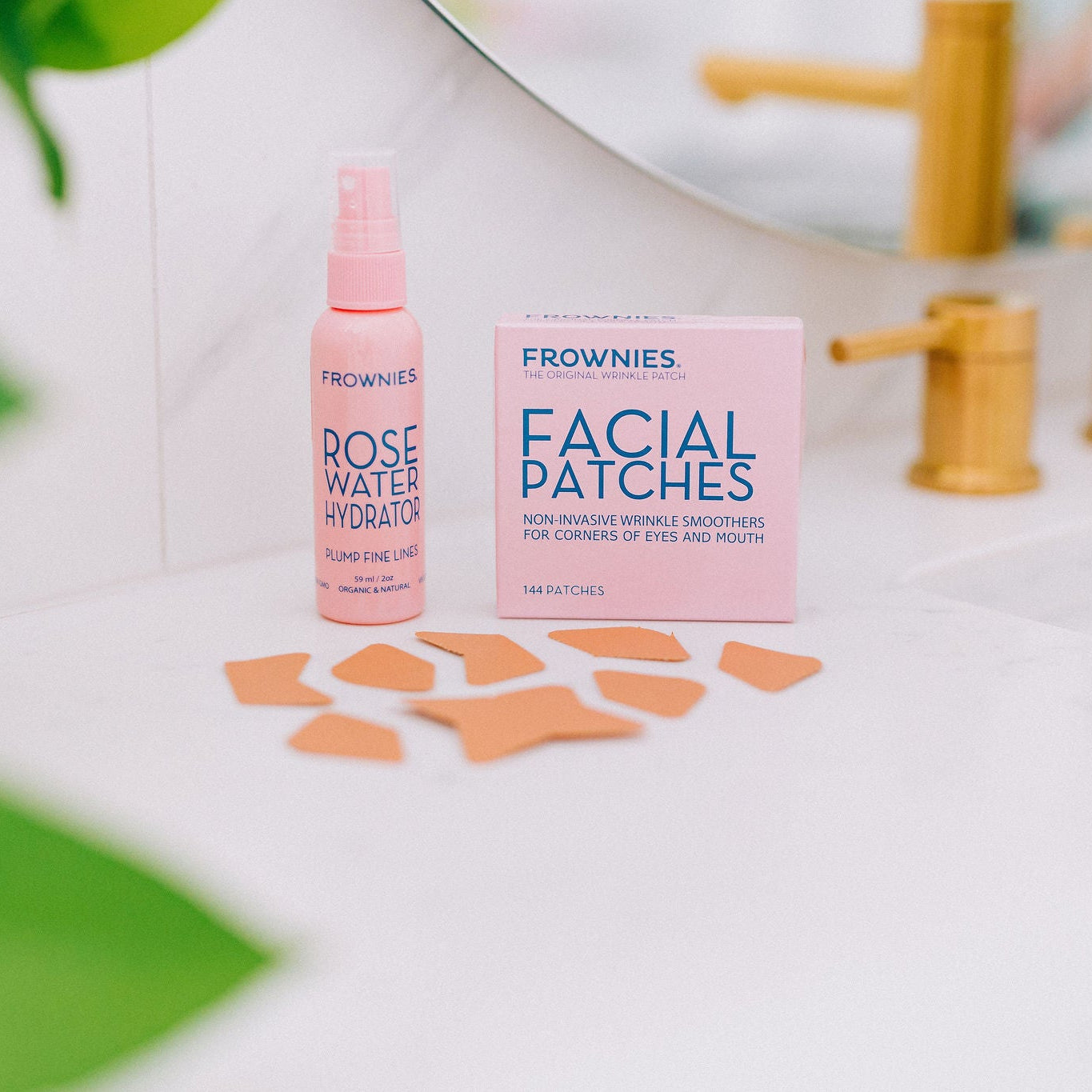 Frownies rose water hydrator spray that is used to plump fine lines and CEM facial patches shown pictured next to each other. The patches are laid out on the bathroom countertop top as well.