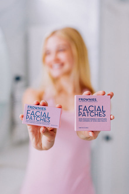 A white woman with blonde hair shown holding Frownies facial patches in both her hands. One box if FBE and the other CEM