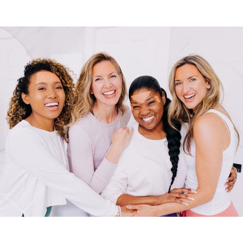 Four women smiling and laughing while demonstrating how to apply Frownies facial patches by wearing them in the picture