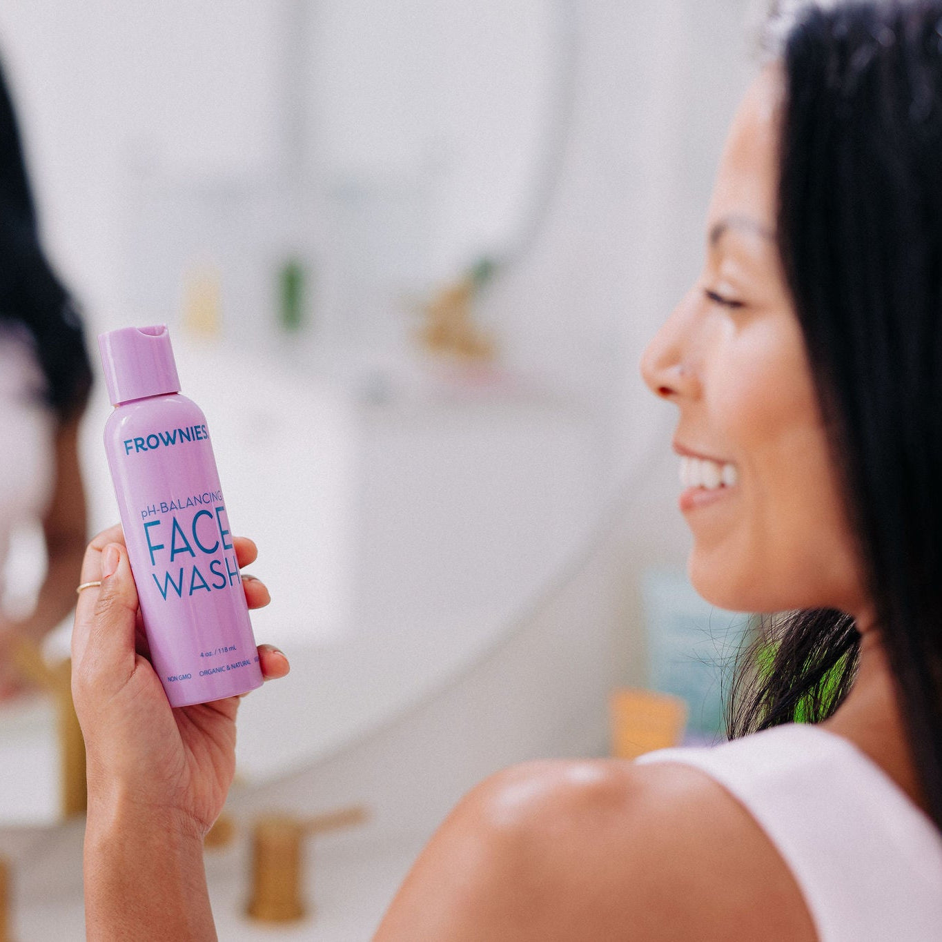 A woman with black hair pictured holding Frownies PH balancing face wash 