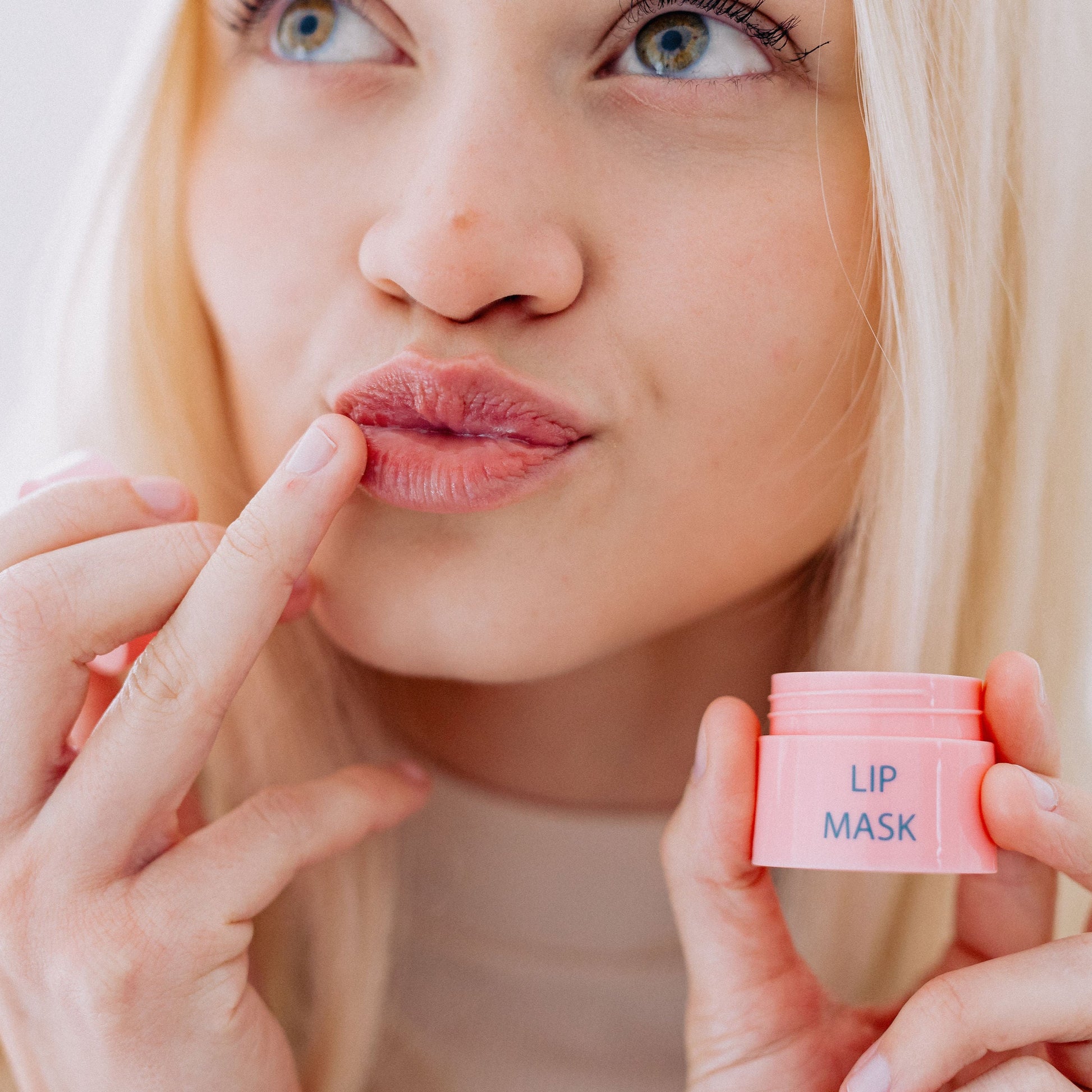 A woman with blonde hair applying the Frownies lip mask to her lips 