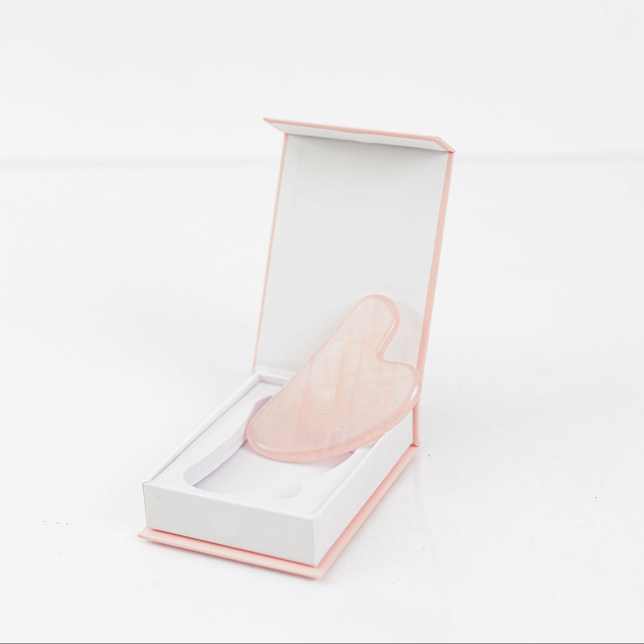 Frownies Gua Sha rose quartz shown in its box on a clean white background