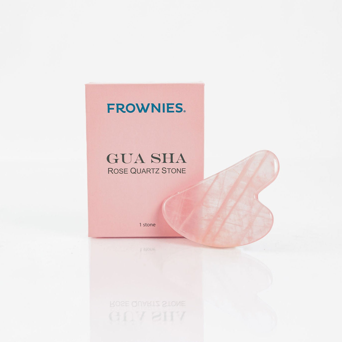 Frownies Gua Sha Rose Quartz Stone outside its box to the right of it on a clean white background 