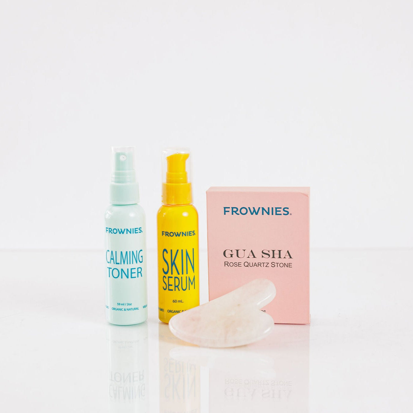 Frownies gua sha rose quartz stone next to Frownies calming toner and skin serum