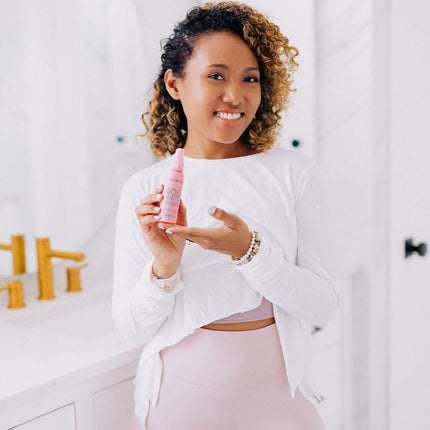 Frownies rose water hydrator spray shown being held by a black woman with curly hair, she is pictured in a bathroom setting 