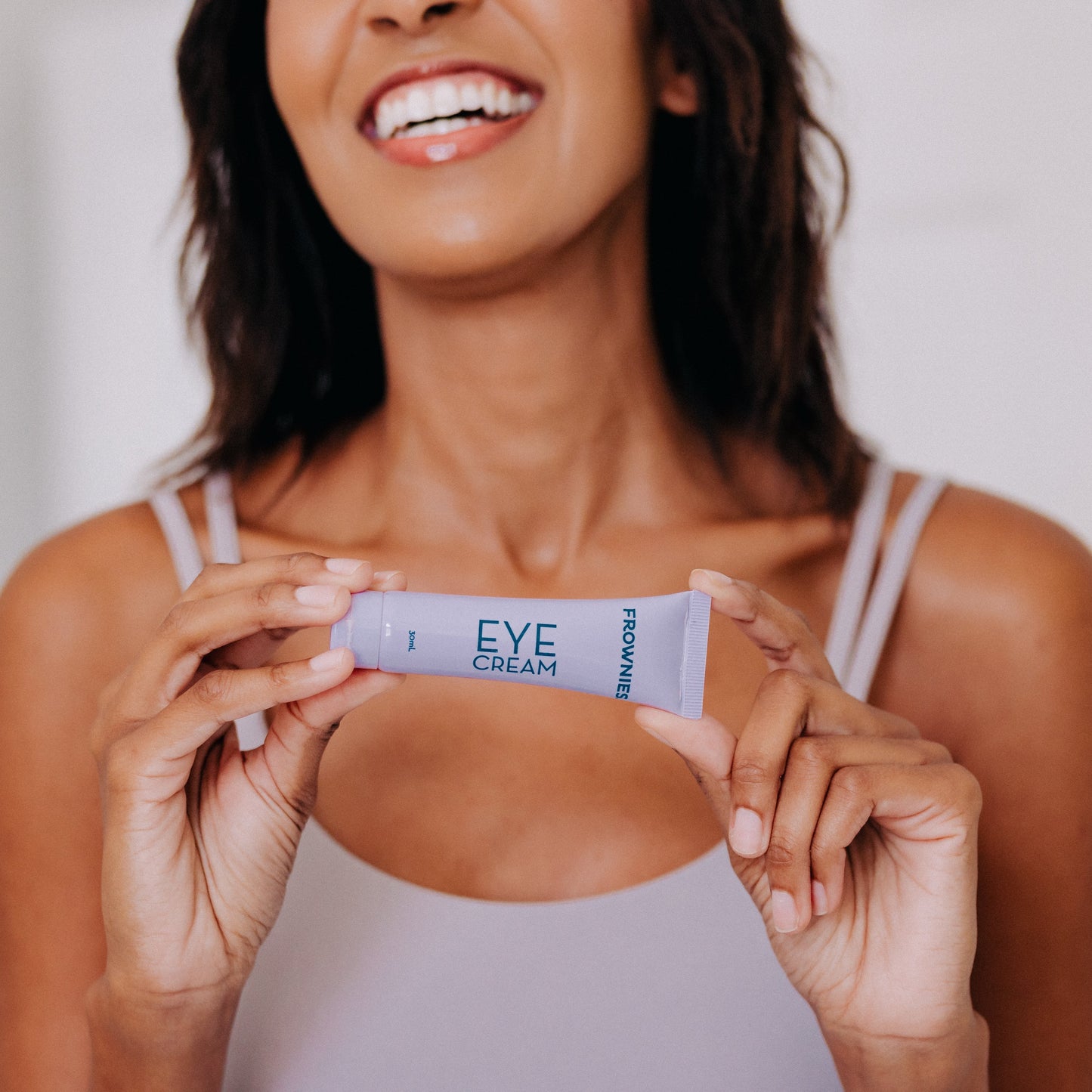 Frownies eye cream being held by a smiling black woman