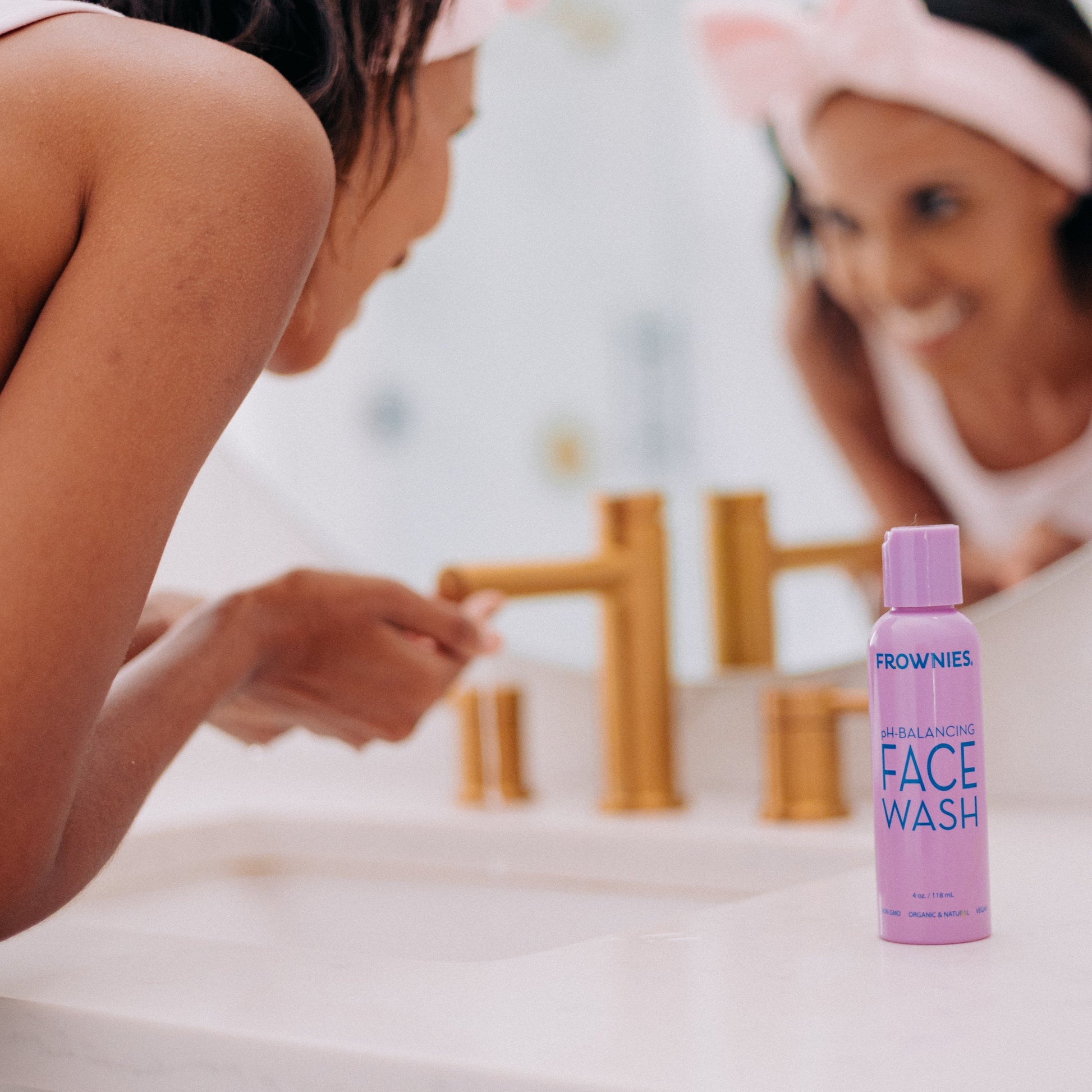 A woman shown washing her face in the sink with Frownies PH balancing face wash next to the sink 