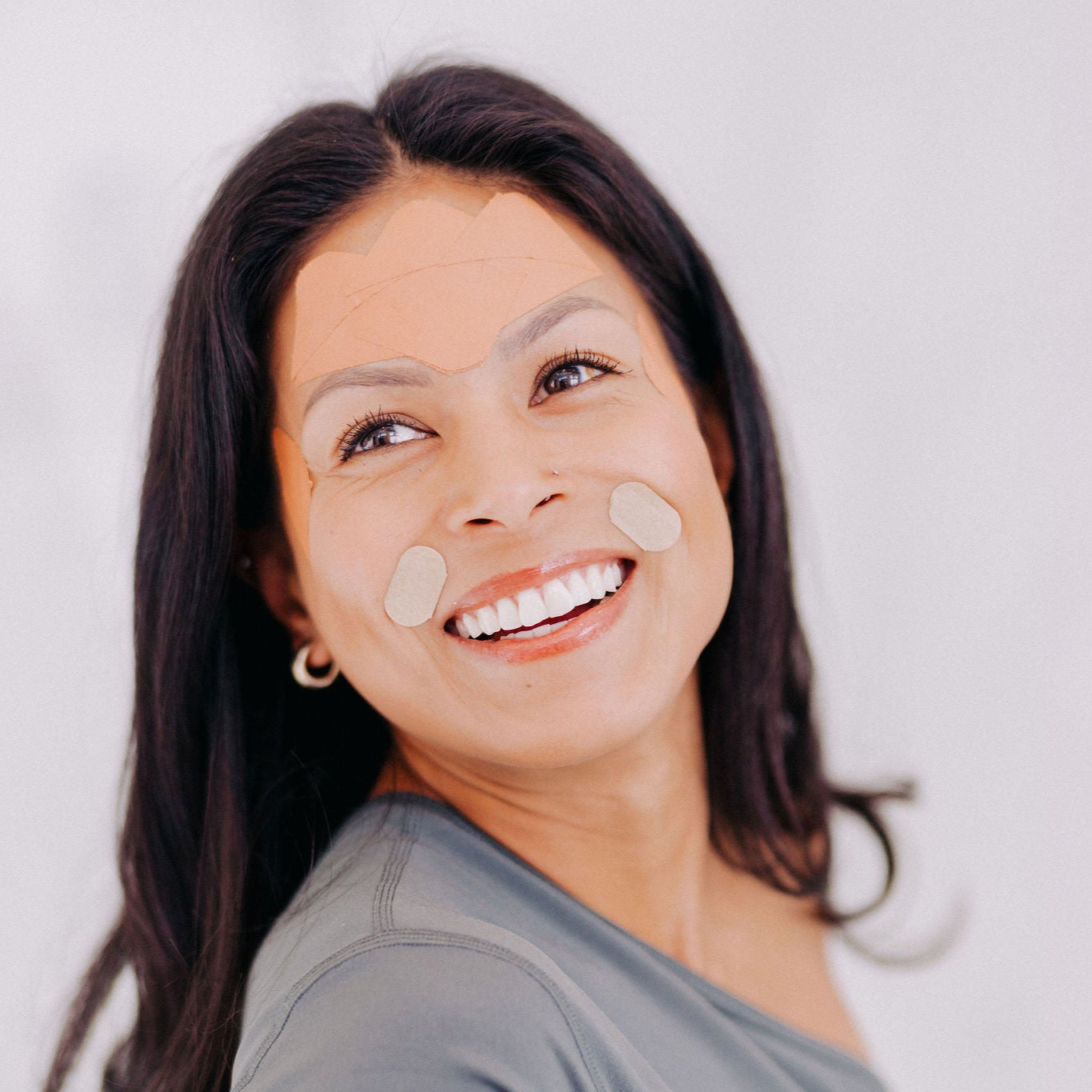 A woman with black hair shown wearing Frownies FBE facial patches and gentle lifts