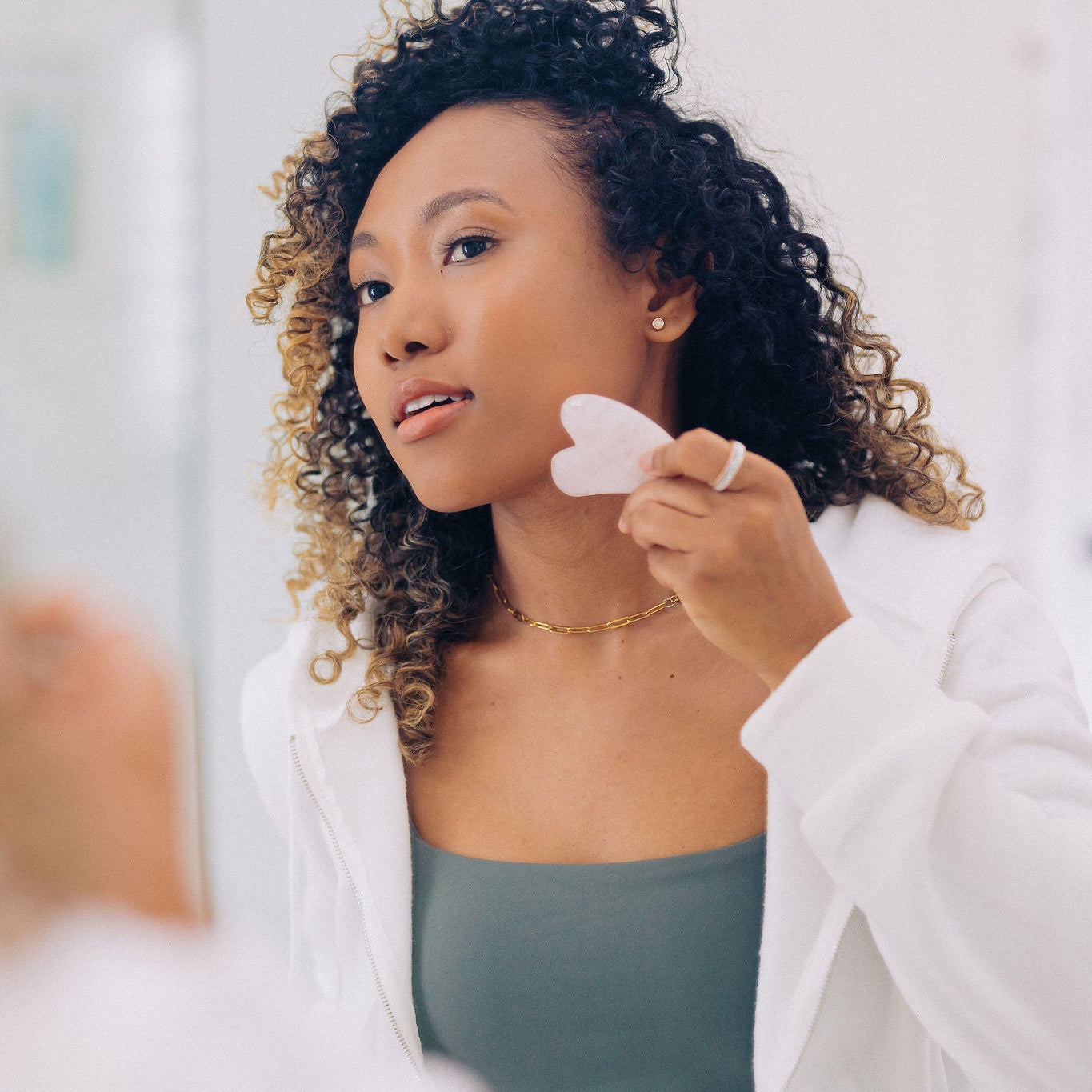 Frownies Gua Sha rose quartz stone being used by a black woman with curly hair 