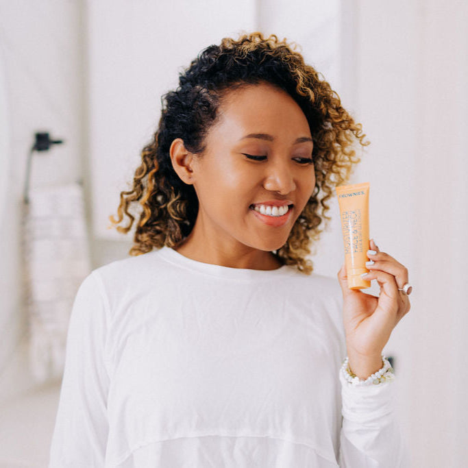 A black woman with curly hair shown holding Frownies moisturizer for face and neck 