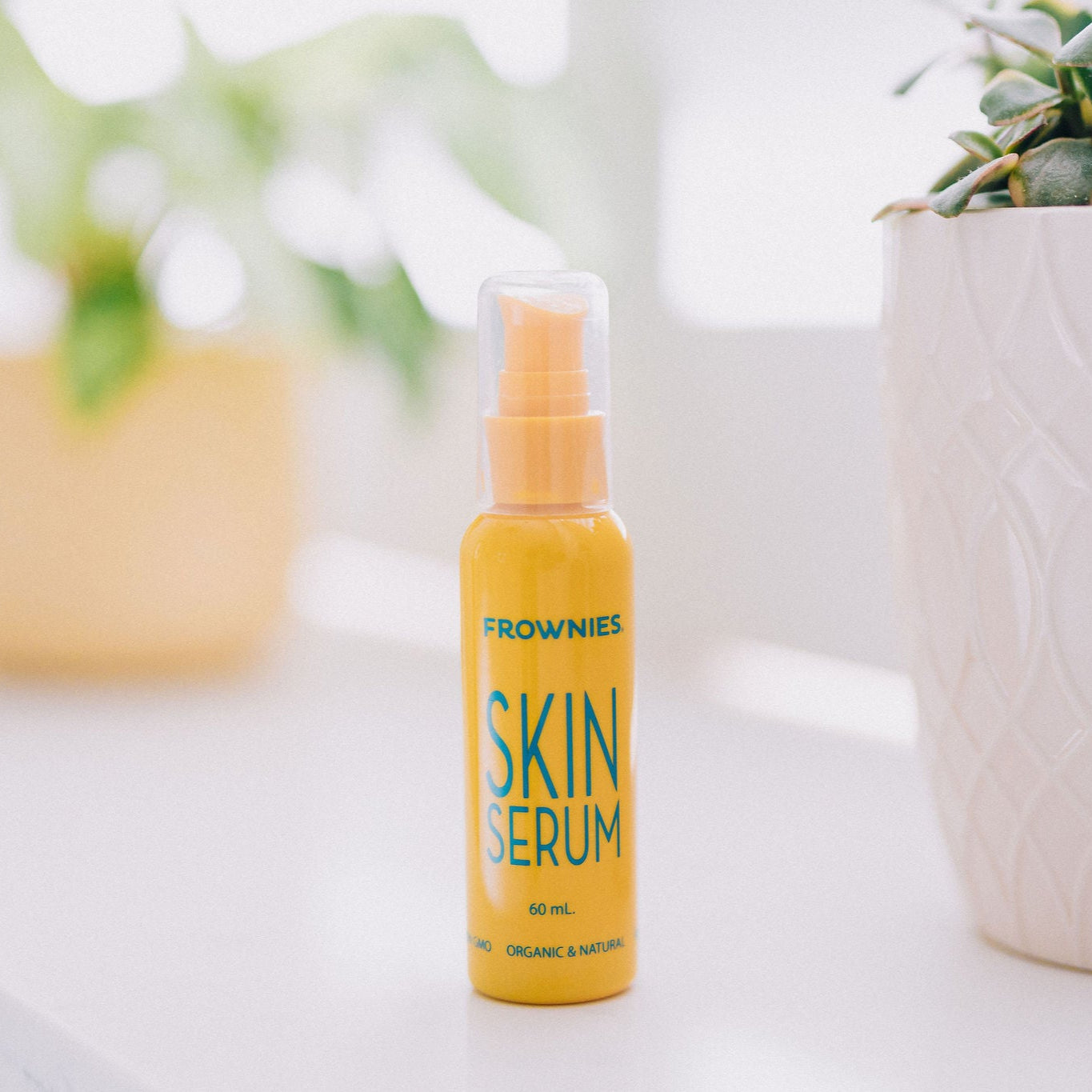 Frownies skin serum bottle shown pictured with some blurred plants in the background