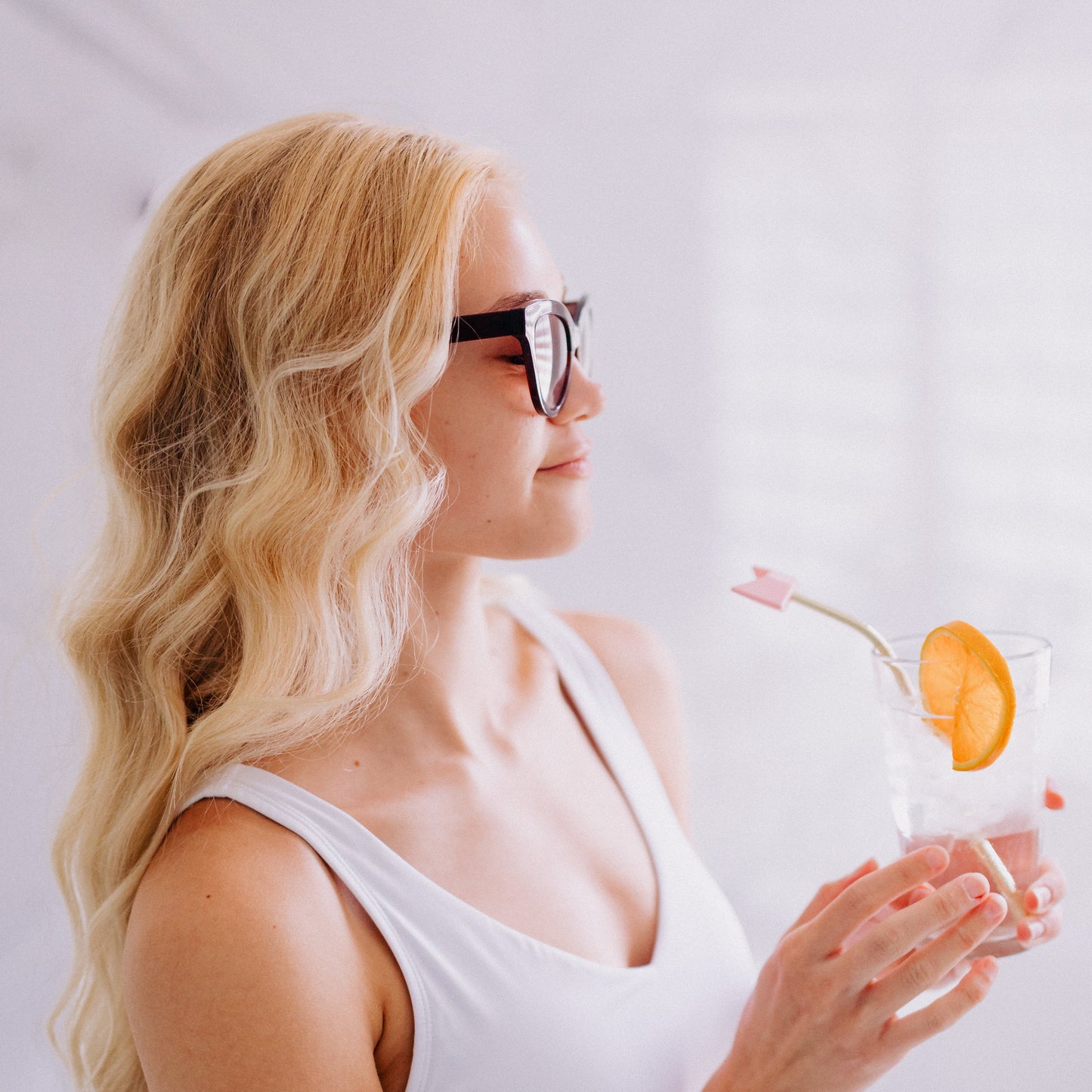 A woman with blonde hair and sunglasses drinking a drink using Frownies wrinkies straw tip