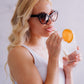 A woman with blonde hair and sunglasses drinking a drink using Frownies wrinkies straw tip