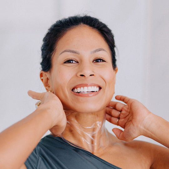 A smiling woman wearing a Frownies apple serum neck mask