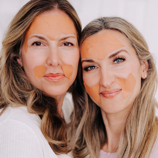 Close-up of two smiling women wearing Frownies facial patches, demonstrating how to properly apply and wear them.