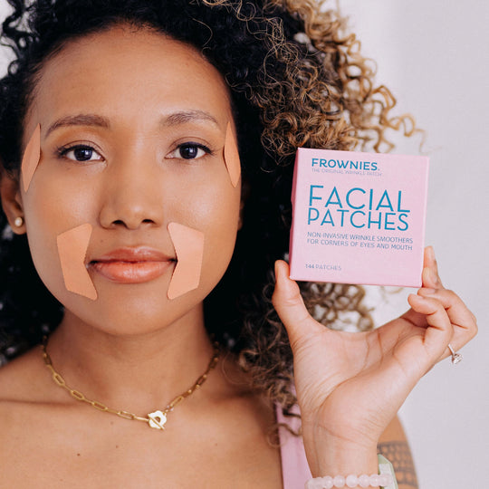 A woman model holding and wearing Frownies CEM (Corners of Eyes and Mouth) facial patches, with the packaging visible in her hand.