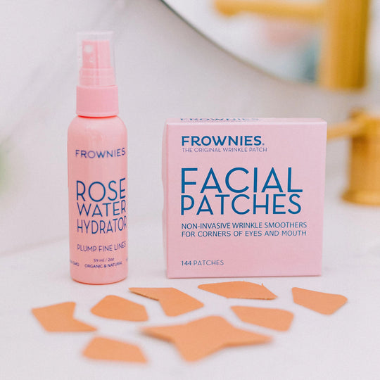 Frownies CEM (Corners of Eyes and Mouth) facial patches and a bottle of rose water hydrator displayed together on a bathroom sink, with additional facial patches laid out nearby.