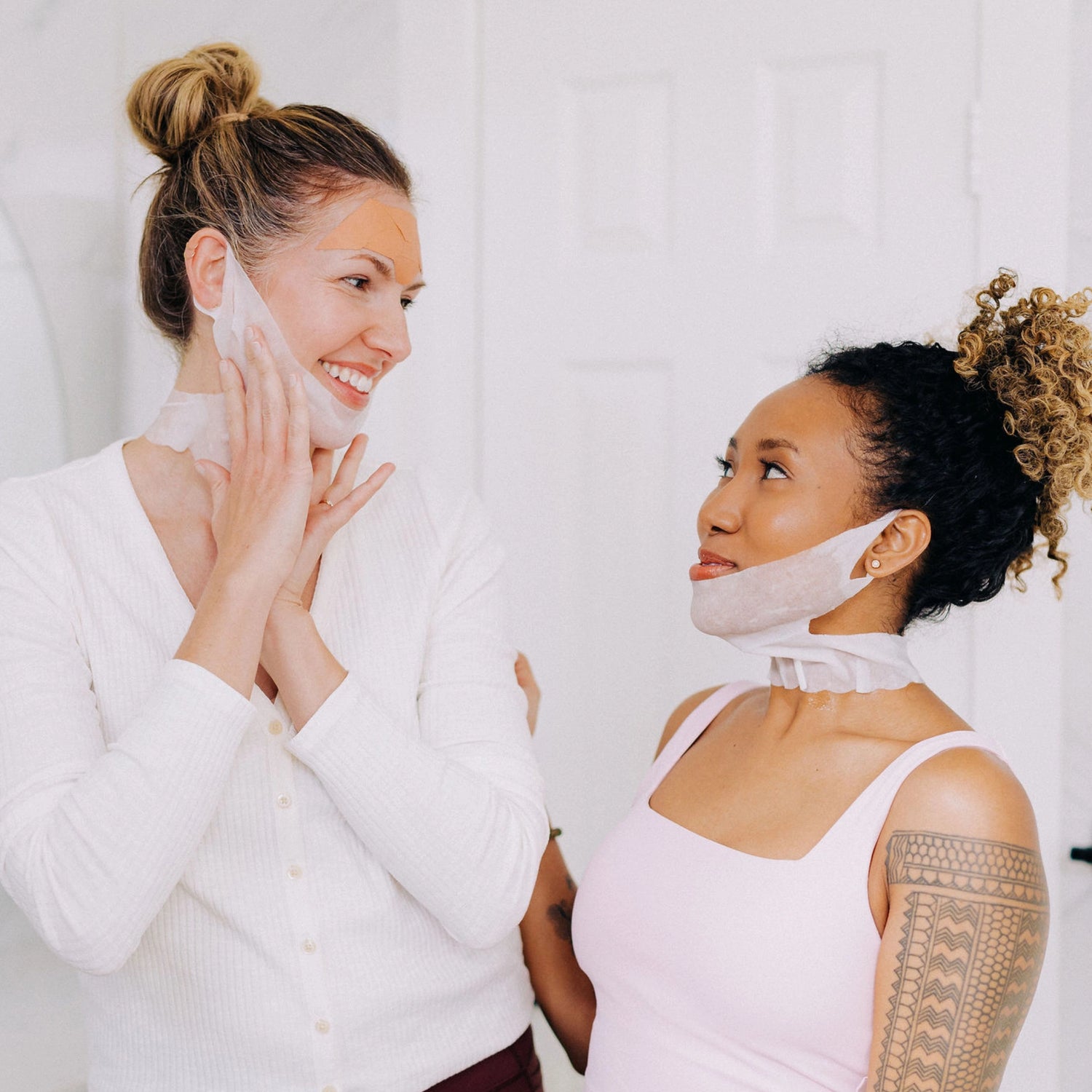 Two women looking at each other and smiling while wearing Frownies Chin-Up Polypeptide Masks.