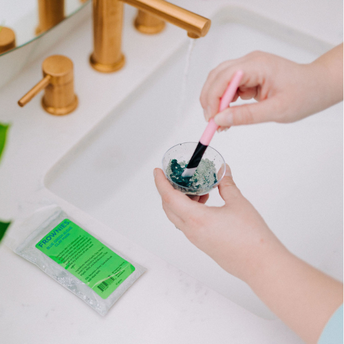 Frownies blue green algae clay mask shown being stirred in the cup to create the final form of the mask before it is applied to the skin 