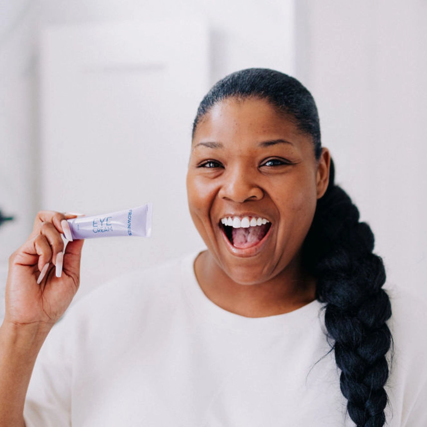 Woman with her mouth open in excitement, holding up Frownies Eye Cream 