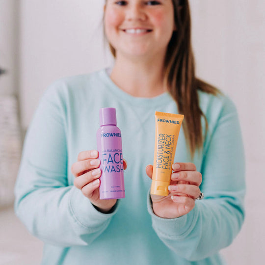 A smiling model holding Frownies face wash and moisturizer for face and neck, presenting the products to the camera.