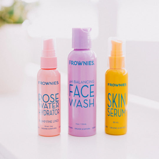 Frownies pH-balancing face wash displayed alongside rose water hydrator and skin serum on a flat surface.