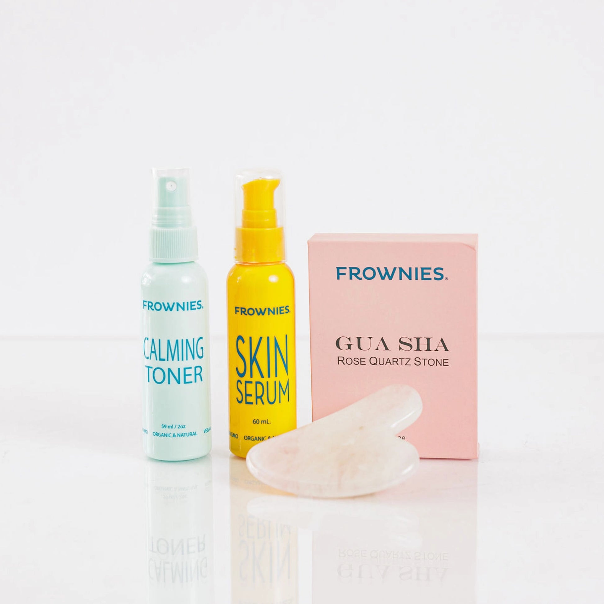 Frownies calming toner, skin serum, and Gua Sha rose quartz stone displayed together on a clean white background.