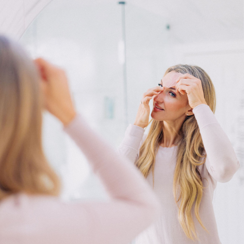 Frownies Gua Sha rose quartz being used by a woman while she is looking in the mirror