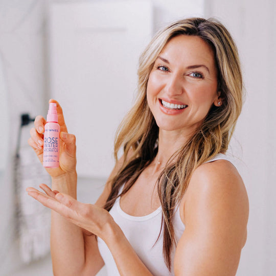 A smiling woman showcasing her Frownies rose water hydrator spray.