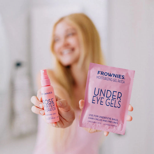 Girl with blonde hair holding Frownies under eye gels in her left hand and rose water hydrator spray in her right hand, with her face and background blurred to emphasize the products.