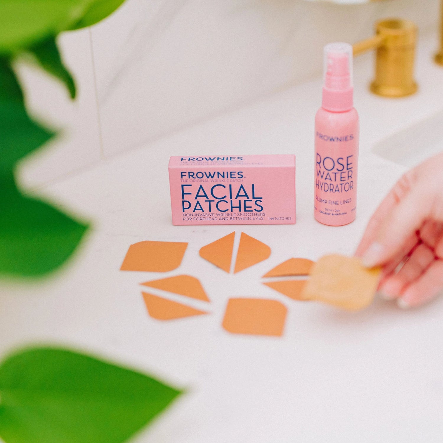 Frownies Forehead and Between Eyes (FBE) facial patches displayed outside of their packaging alongside a rose water hydrator.