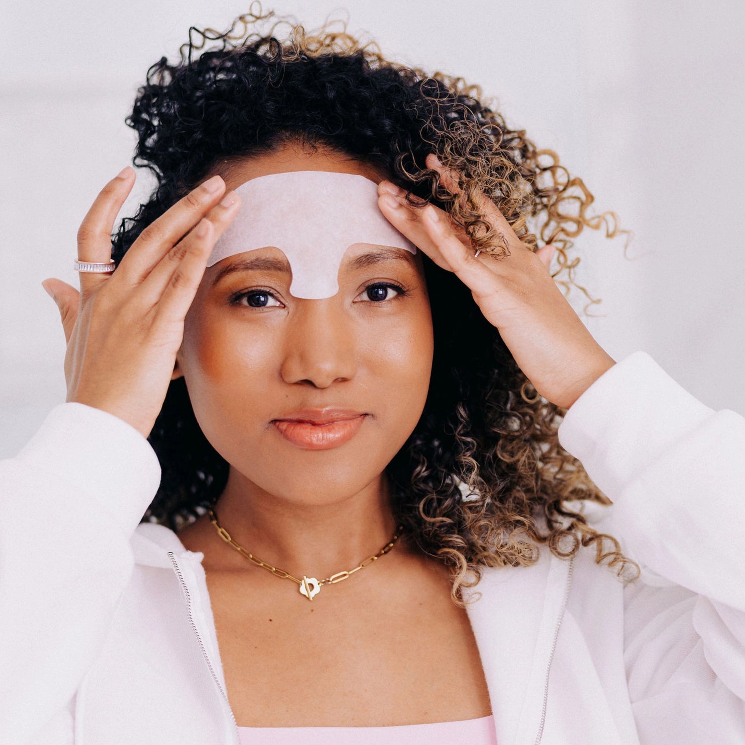 A happy woman with curly hair smirking while wearing a Frownies forehead serum patch.