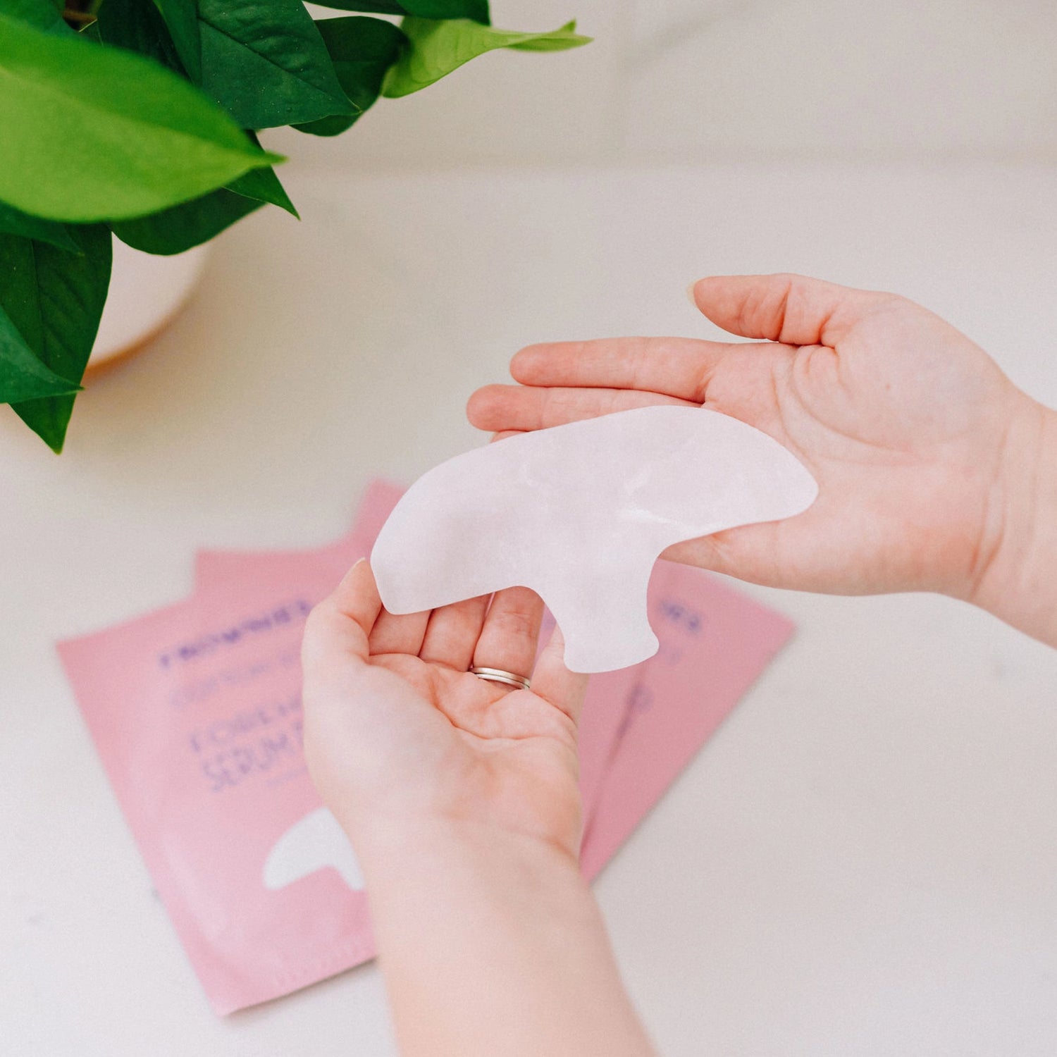 Hands holding a Frownies forehead serum patch, with the packaging visible on the table beneath.